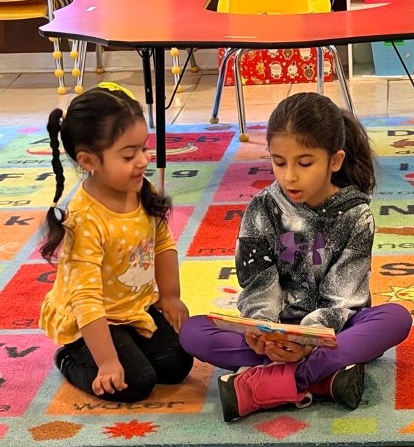 Two children reading a picture book together on the alphabet rug