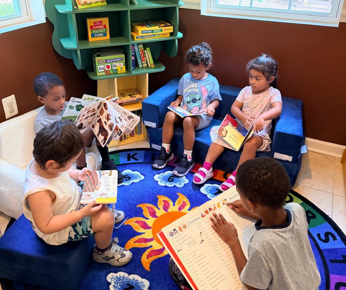 Four children reading picture books together in the cozy library corner