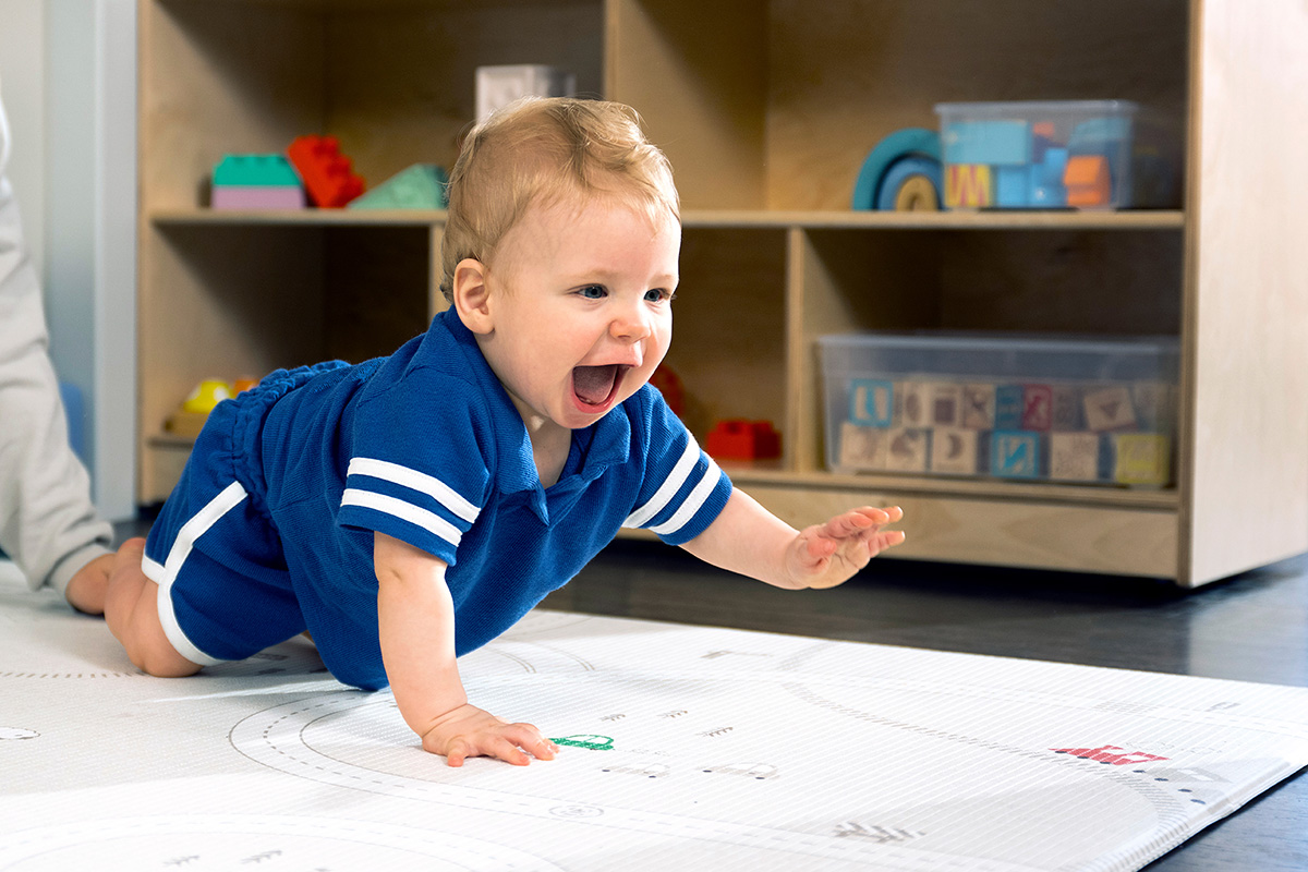 A warm infant and toddler classroom where a caregiver gently engages with two young children